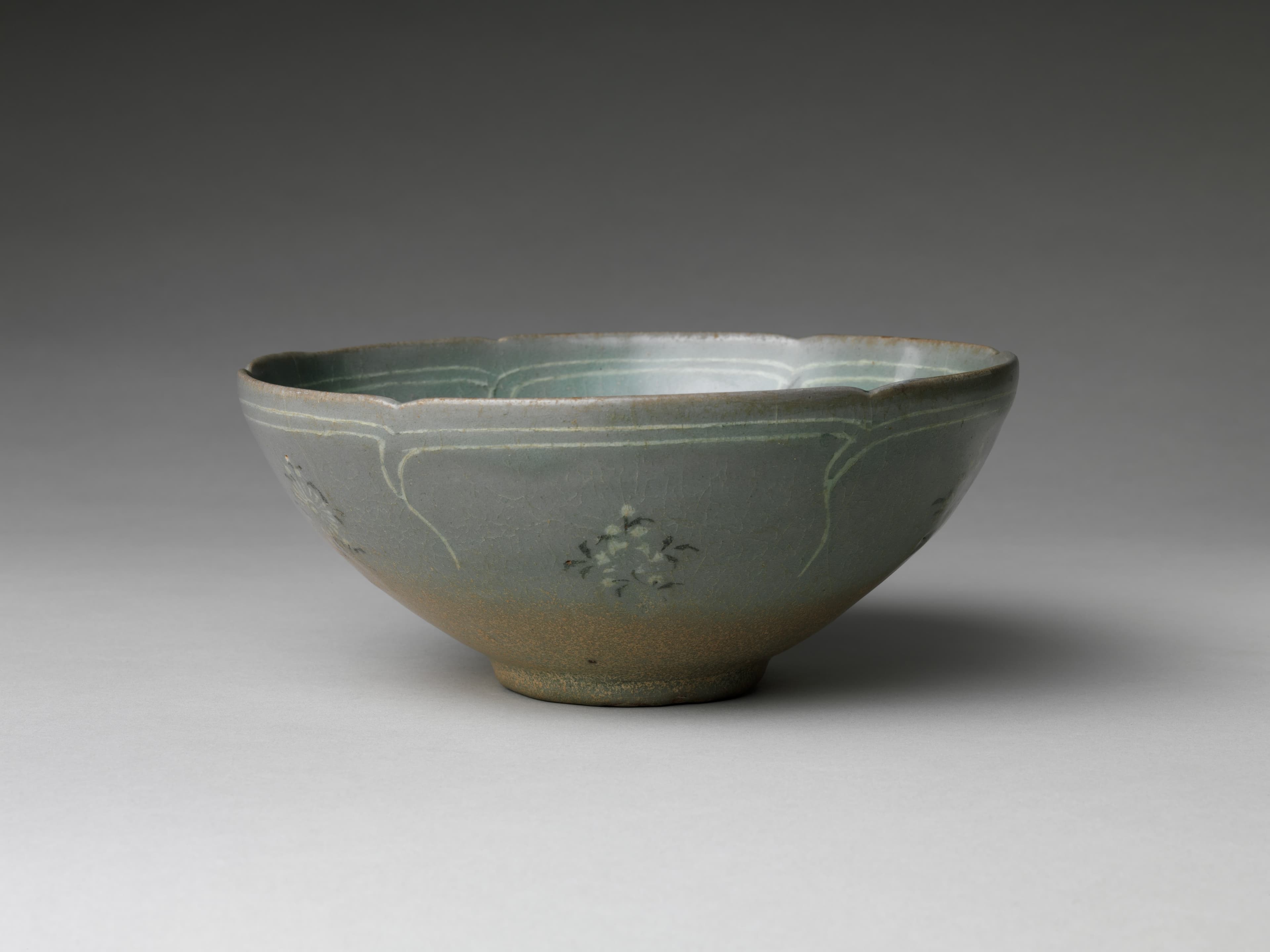 A 12th-century Goryeo celadon bowl with inlaid chrysanthemum and butterfly designs under jade-green glaze, photographed on a dark museum background.